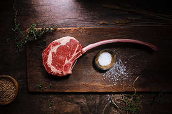 Photo en vue de dessus d'une pièce de viande sur une planche en bois et avec un petit bol de sel.