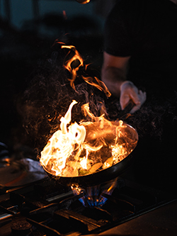 Photo d'un cuisinier en train de faire flamber une poêle.